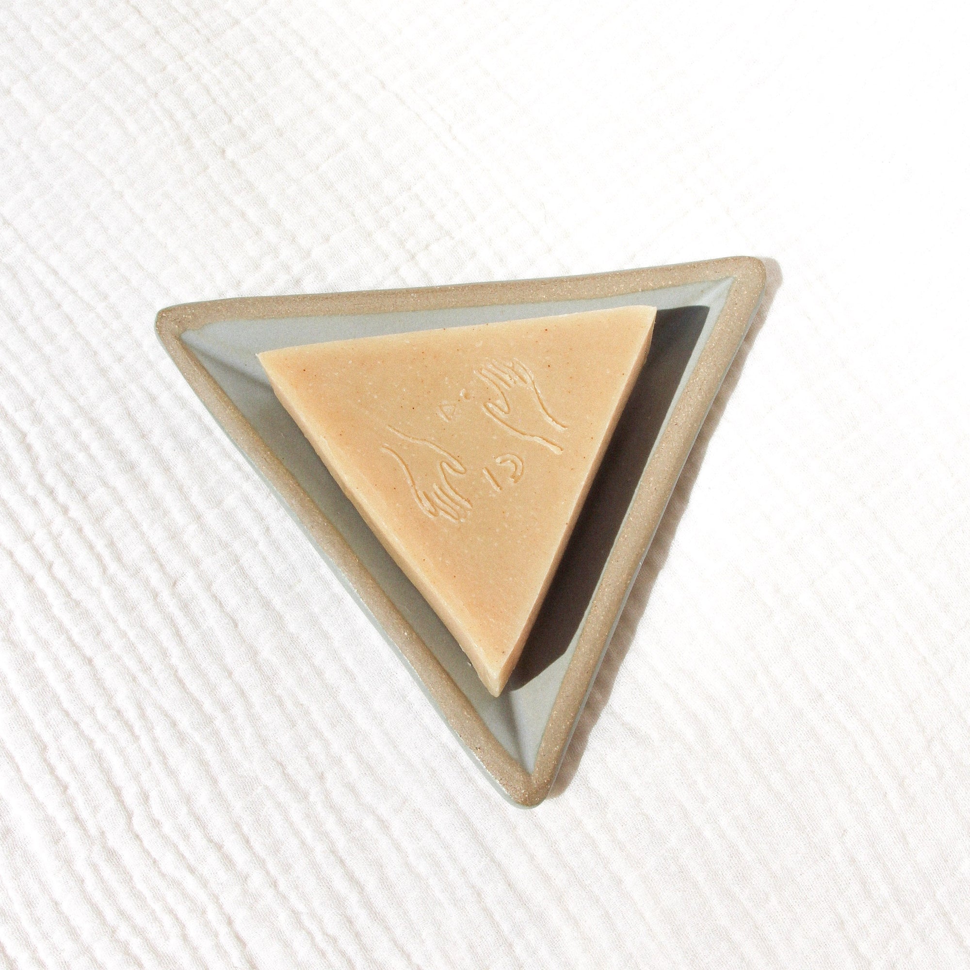 A triangular soap on a triangular soap dish against textured linen