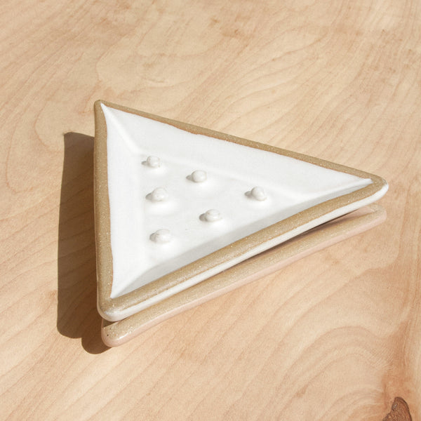 Two triangular ceramic soap dishes against wood grain